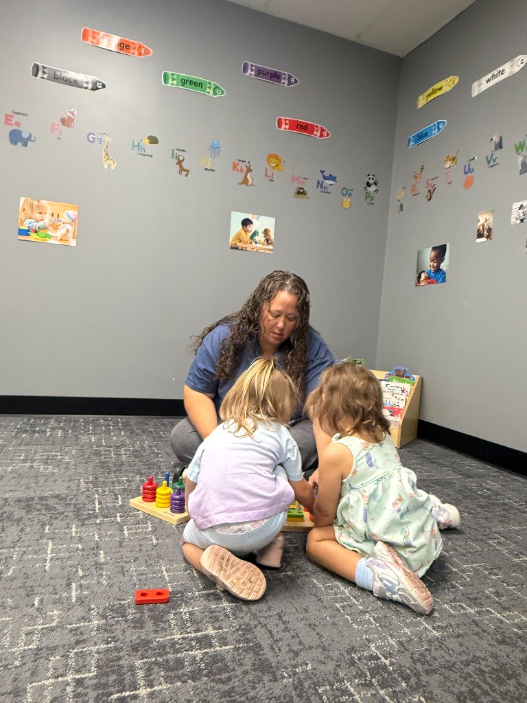 A teacher sitting with young children during floor play with colorful toys at For A Child